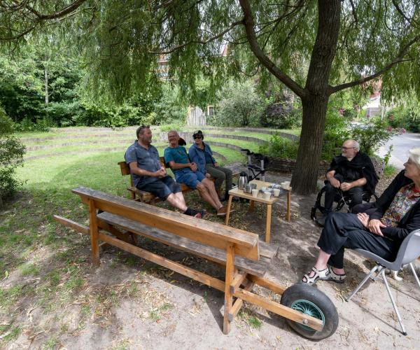 Mensen in gesprek zittend op een bankjes onder een boom